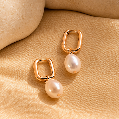 Gold hoop earrings with pearl drops on a beige fabric background