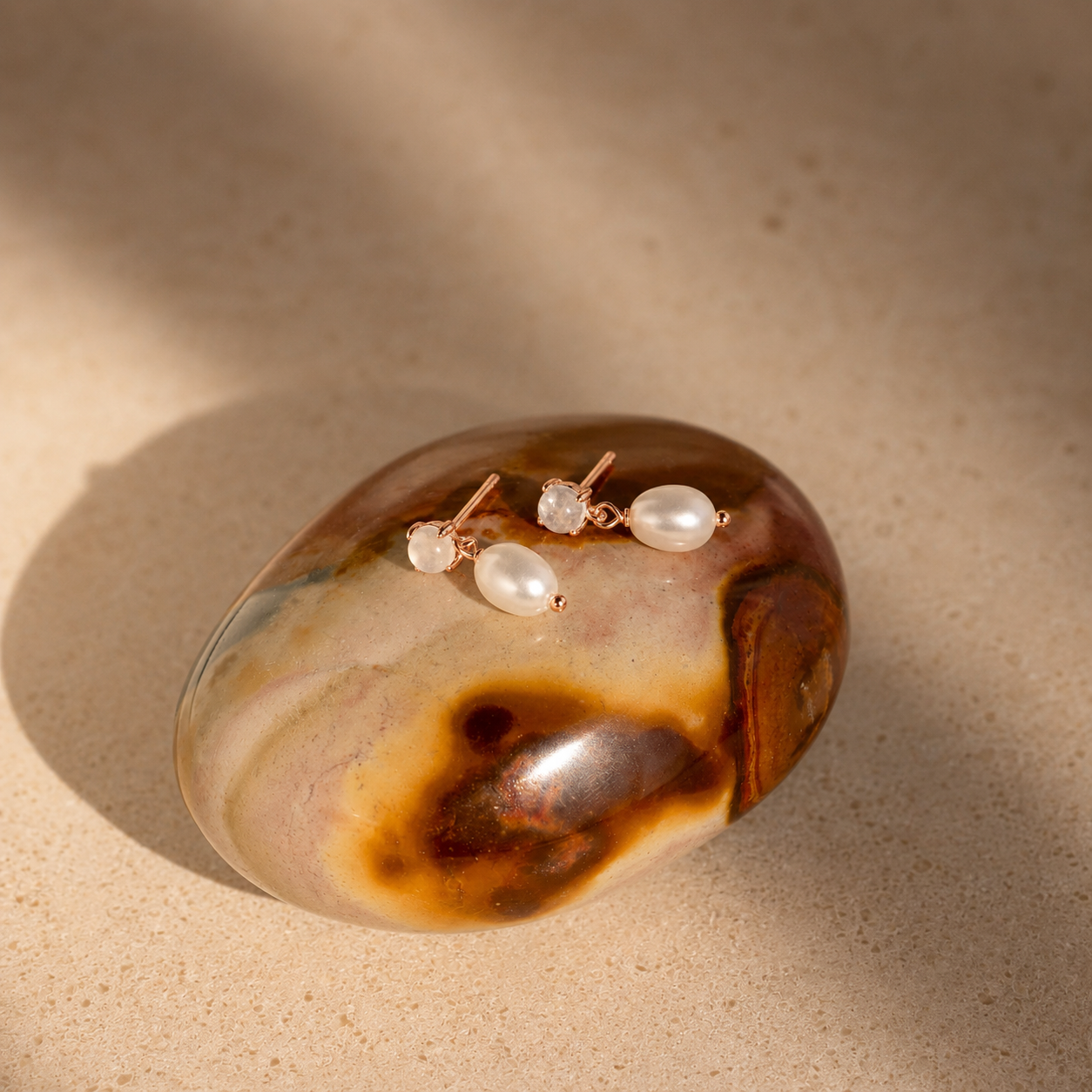 Pair of pearl earrings on a decorative stone with a warm beige background