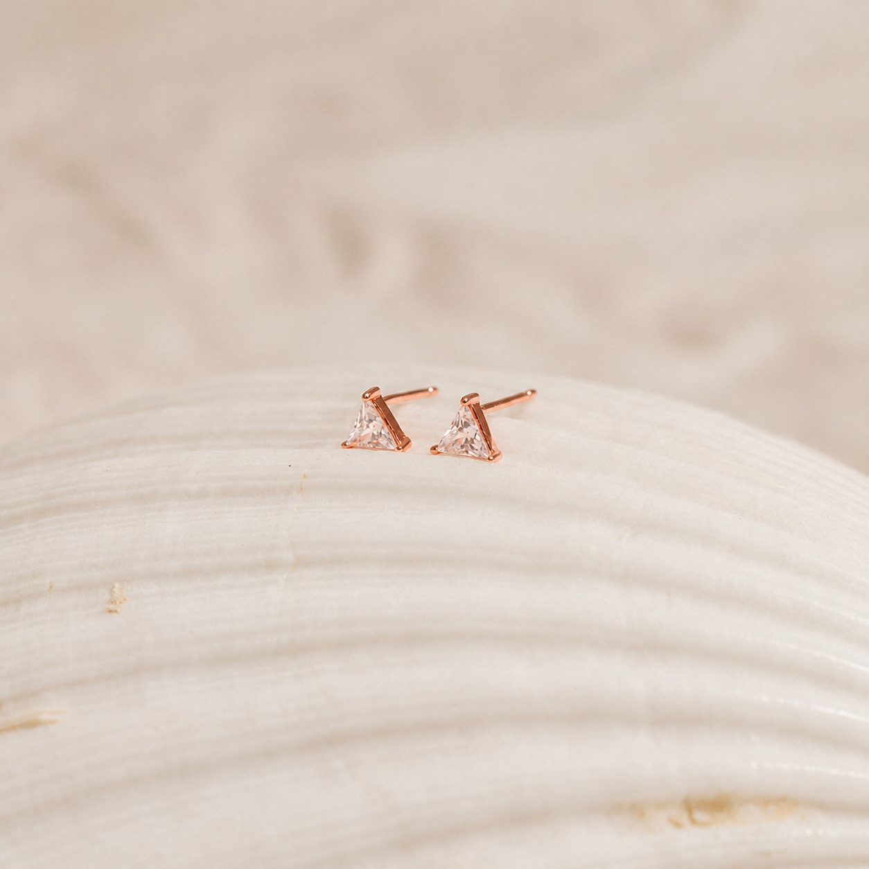 Rose gold earrings with clear gemstones on a textured beige surface