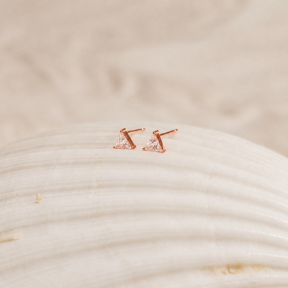 Rose gold earrings with clear gemstones on a textured beige surface