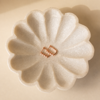 Floral-shaped white soap with a gold clasp on a beige background
