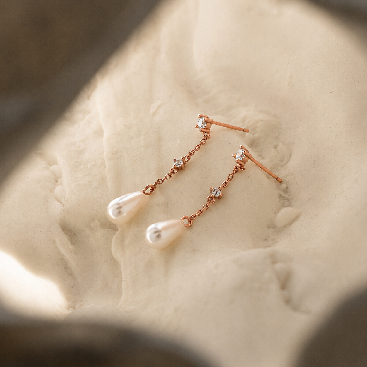 Rose gold earrings with pearls on a textured surface