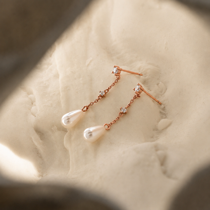 Rose gold earrings with pearls on a textured surface