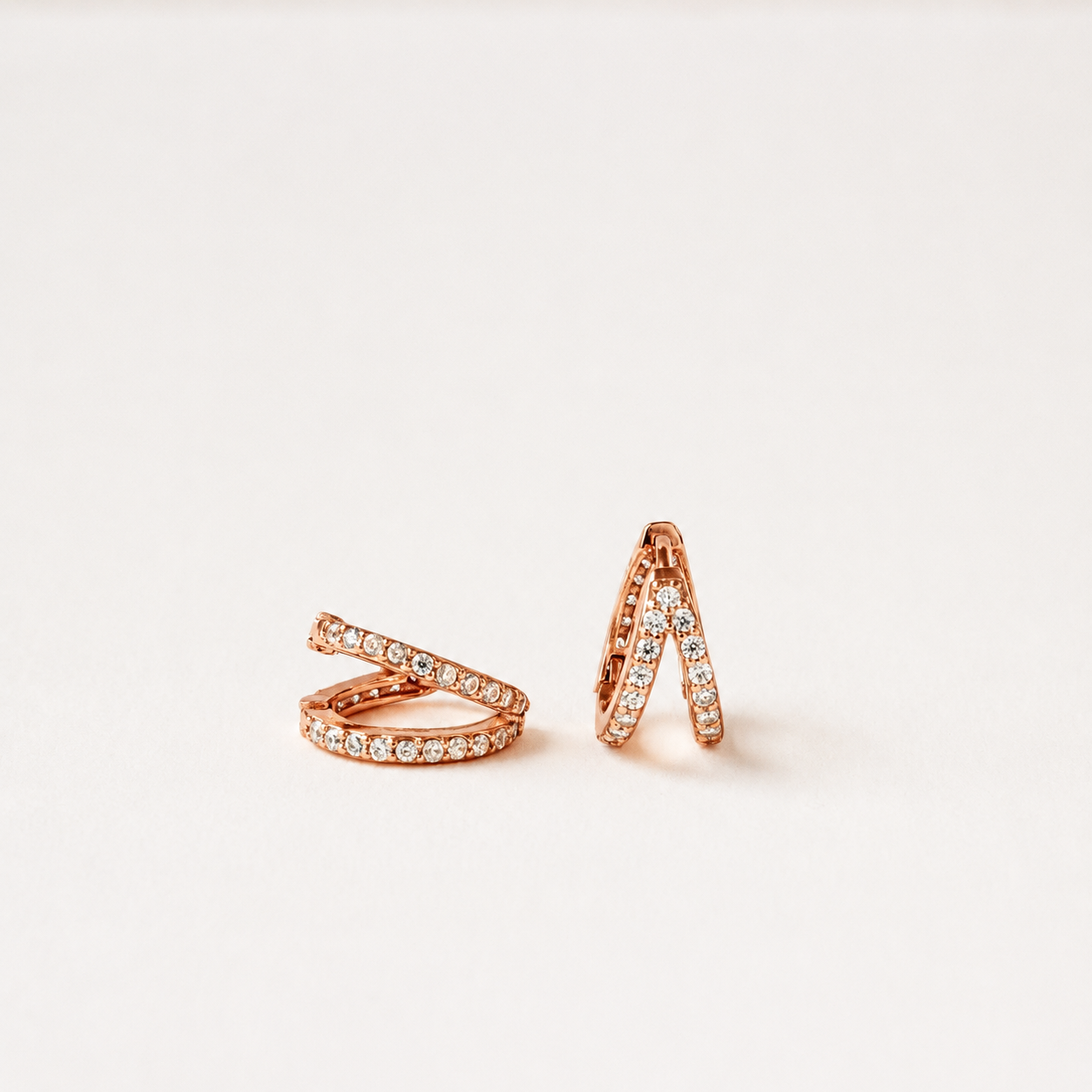 A pair of rose gold wrap-style rings set with small clear stones, displayed on a clean off-white background.