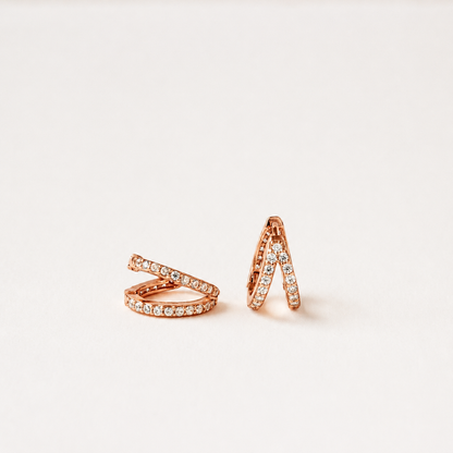 A pair of rose gold wrap-style rings set with small clear stones, displayed on a clean off-white background.