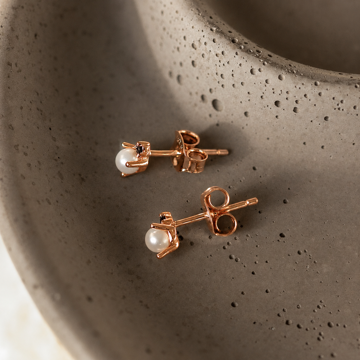 Rose gold earrings with pearls on a textured brown surface