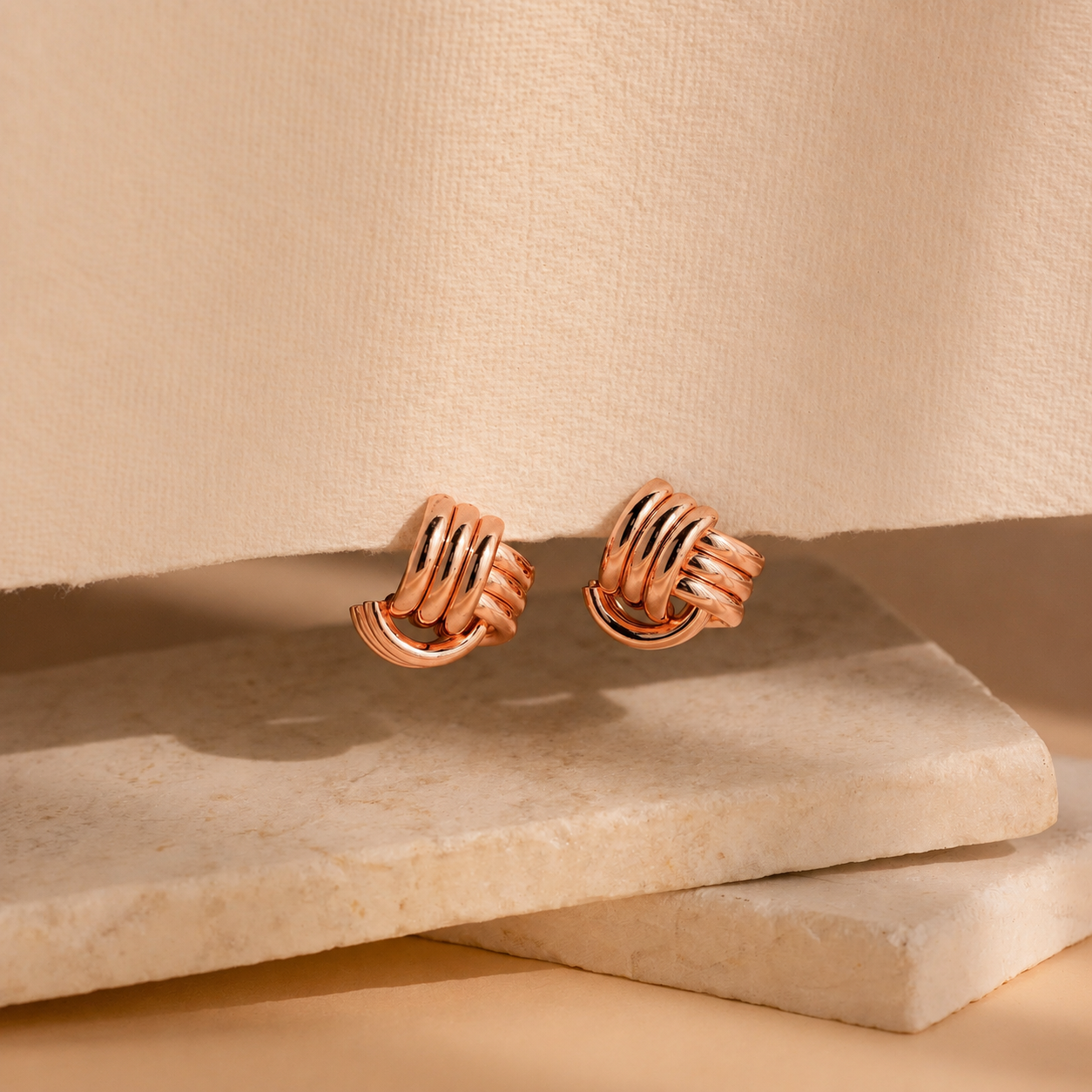 Pair of rose gold earrings on a beige stone surface