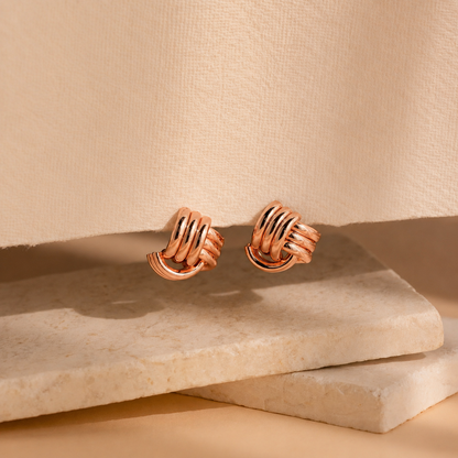 Pair of rose gold earrings on a beige stone surface