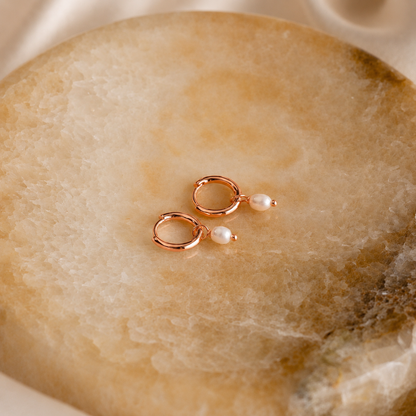 Rose gold earrings with pearls on a stone surface
