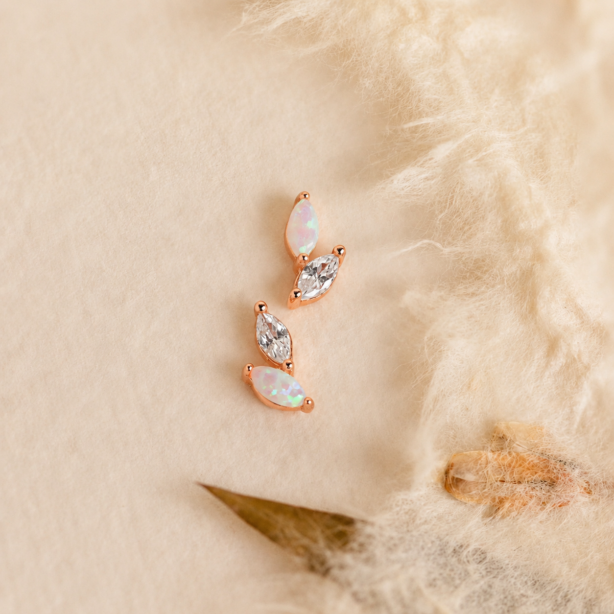 Rose gold earrings with opal and clear gemstones on a soft beige background