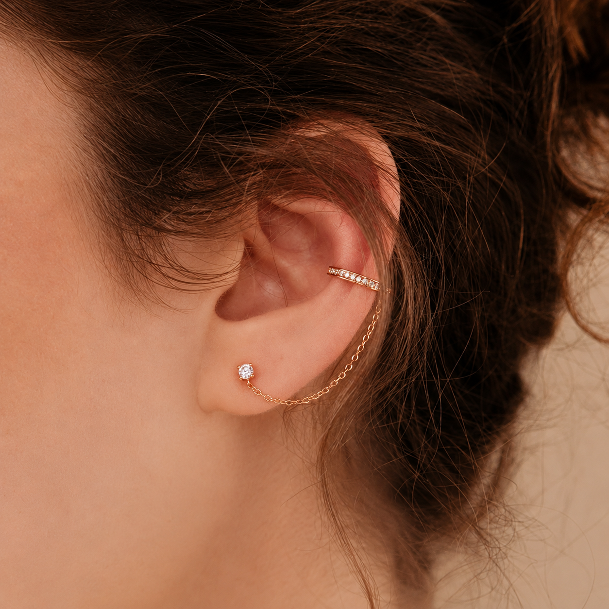 Close-up of an ear wearing a gold earring with a chain design.