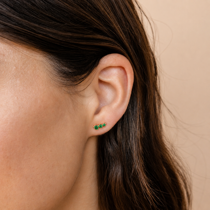 Close-up of an ear wearing green earrings with a neutral background