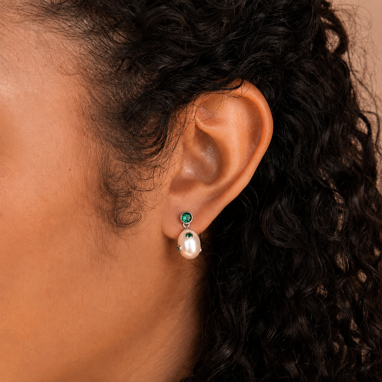 Close-up of an ear wearing a pearl earring with green gemstones.