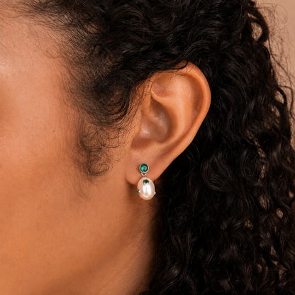 Close-up of an ear wearing a pearl earring with green gemstones.
