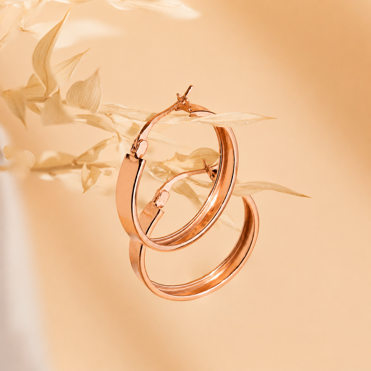 Rose gold hoop earrings on a soft beige background with floral elements
