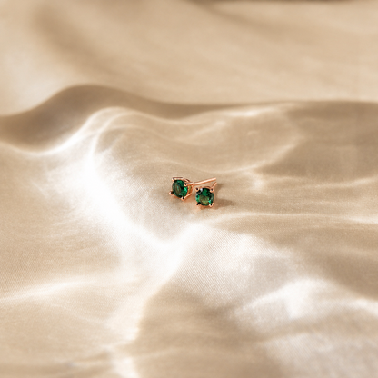 Pair of green gemstone earrings on a beige fabric background