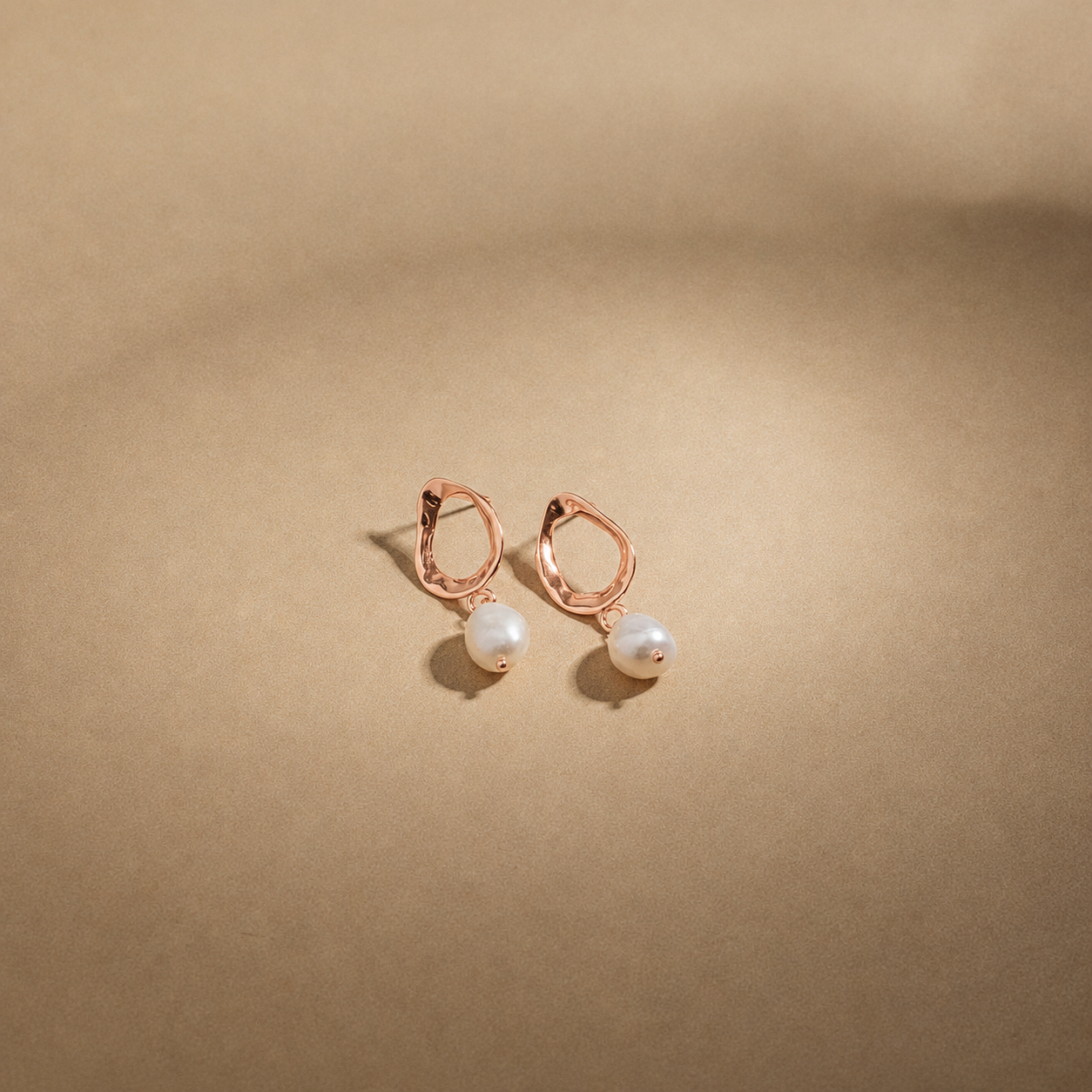 Rose gold earrings with pearl drops on a beige background