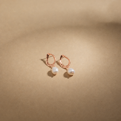 Rose gold earrings with pearl drops on a beige background