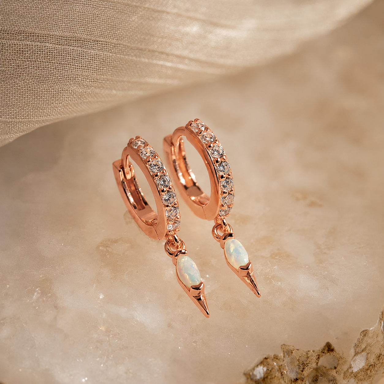 Rose gold hoop earrings with opal stones on a beige fabric background