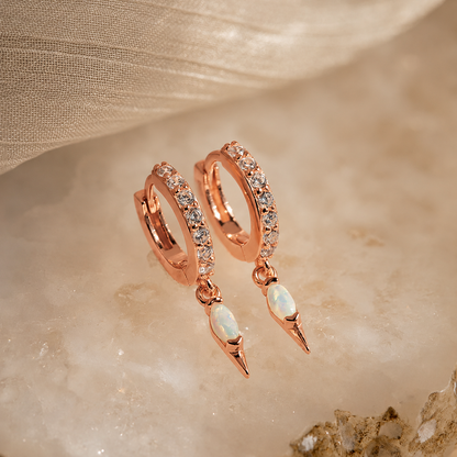 Rose gold hoop earrings with opal stones on a beige fabric background