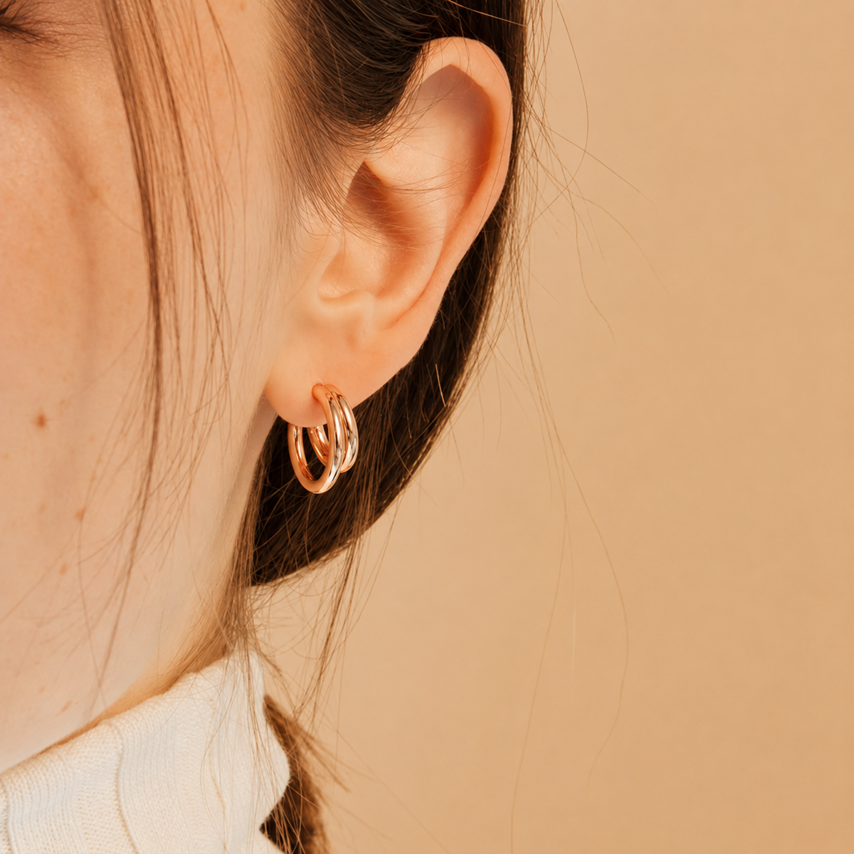 Close-up of an ear wearing a gold hoop earring on a beige background