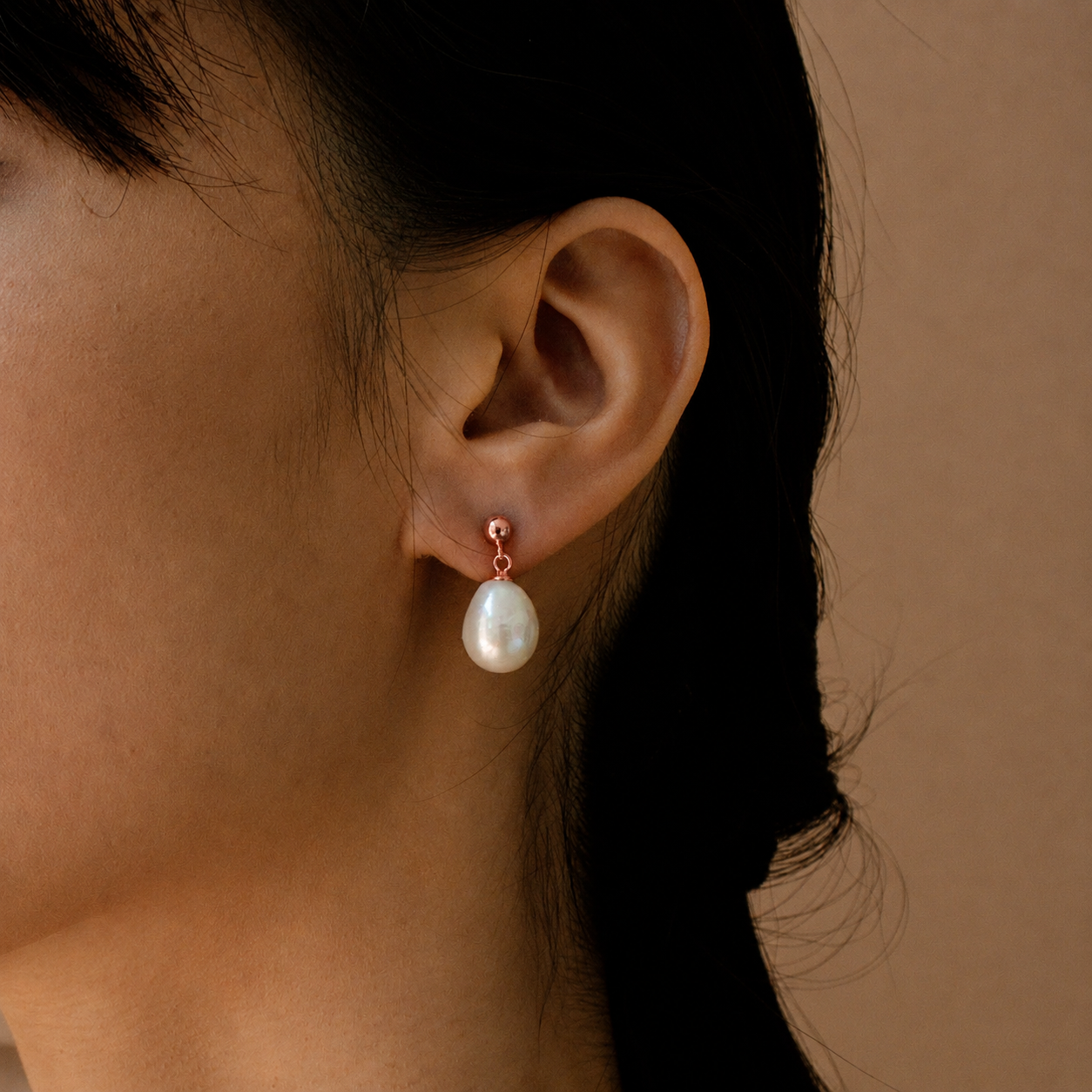 Pearl earring worn by a person against a neutral background