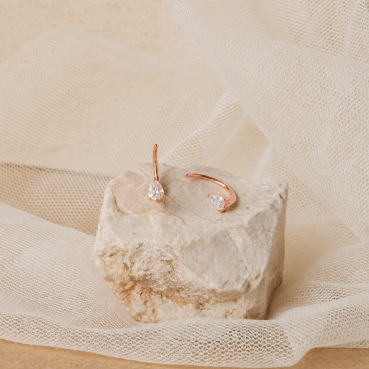 Rose gold earrings with clear gemstones on a textured stone surface