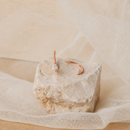 Rose gold earrings with clear gemstones on a textured stone surface