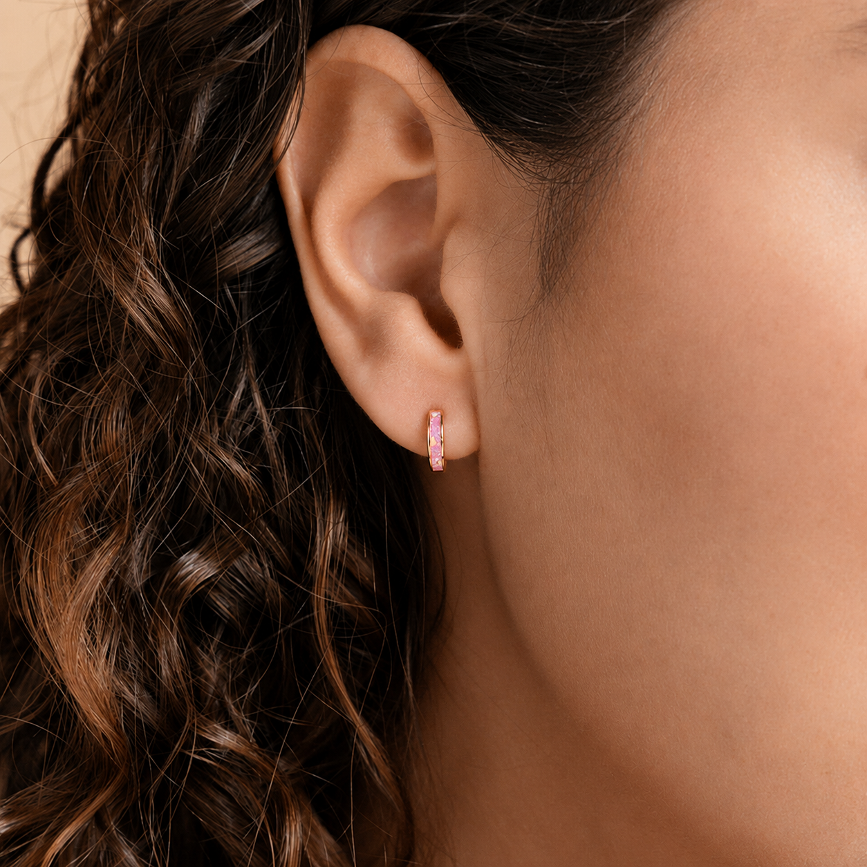 Close-up of an ear wearing a pink hoop earring with wavy hair.