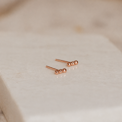 Rose gold stud earrings on a light beige fabric background