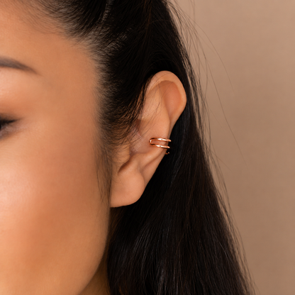 Close-up of a woman's ear wearing a gold earring against a neutral background