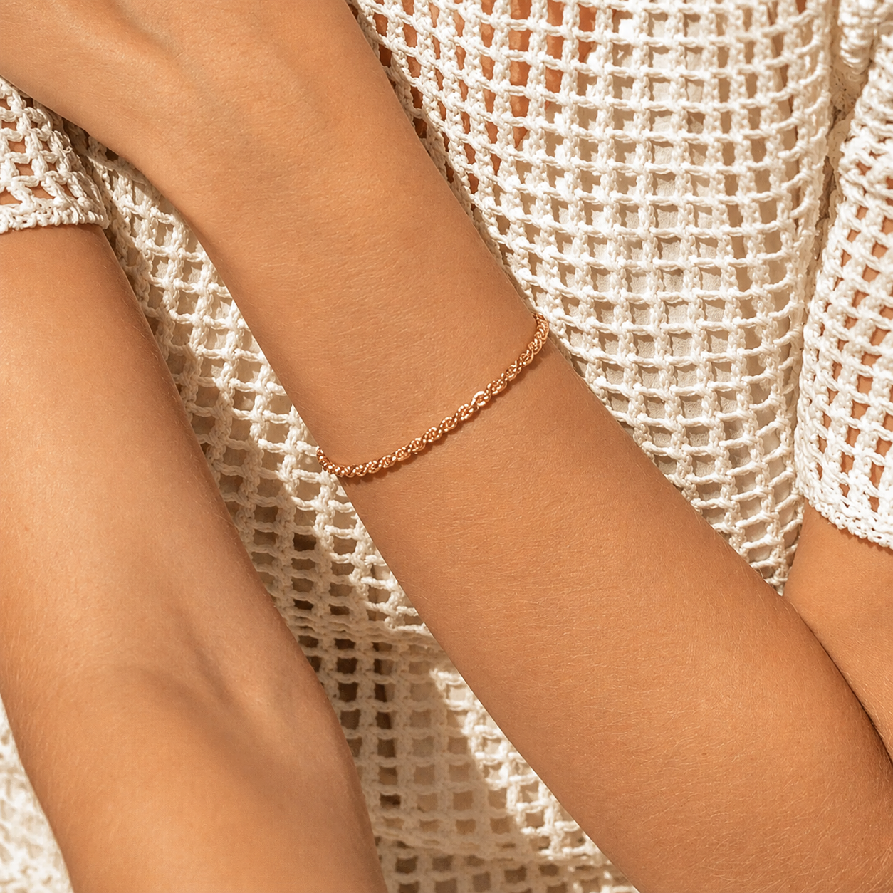 Rose gold bracelet on a person's wrist with a white textured garment in the background
