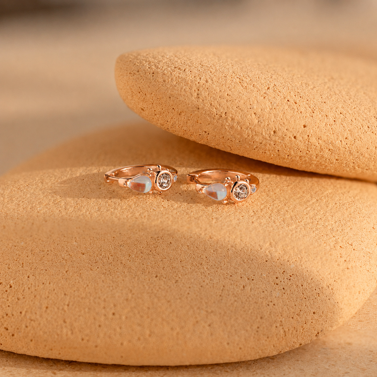 Pair of gold rings with gemstones on a beige stone surface