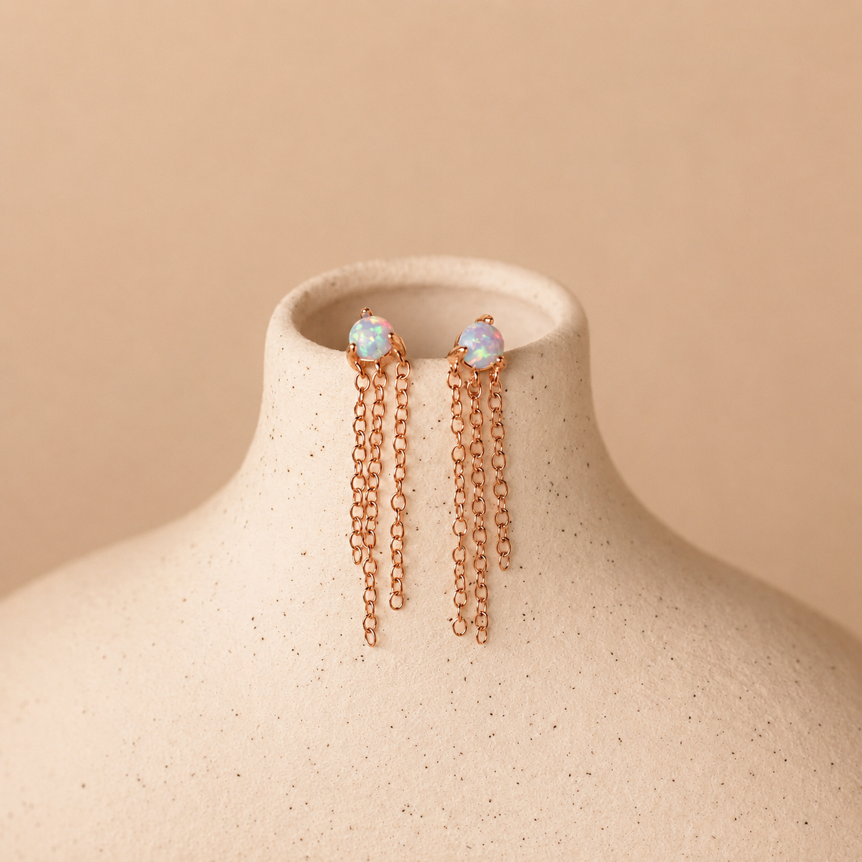 Rose gold earrings with opal stones on a beige mannequin bust.