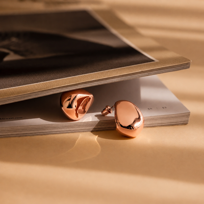 Rose gold earrings on a stack of magazines with a warm beige background