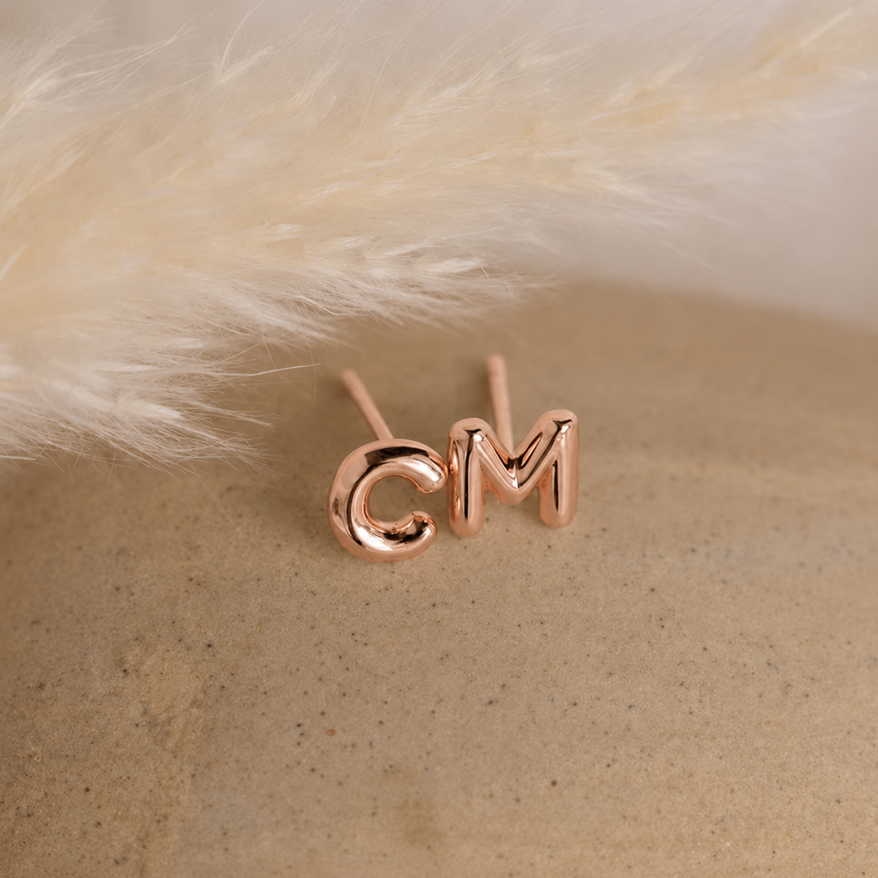 Rose gold earrings with 'CM' on a beige surface