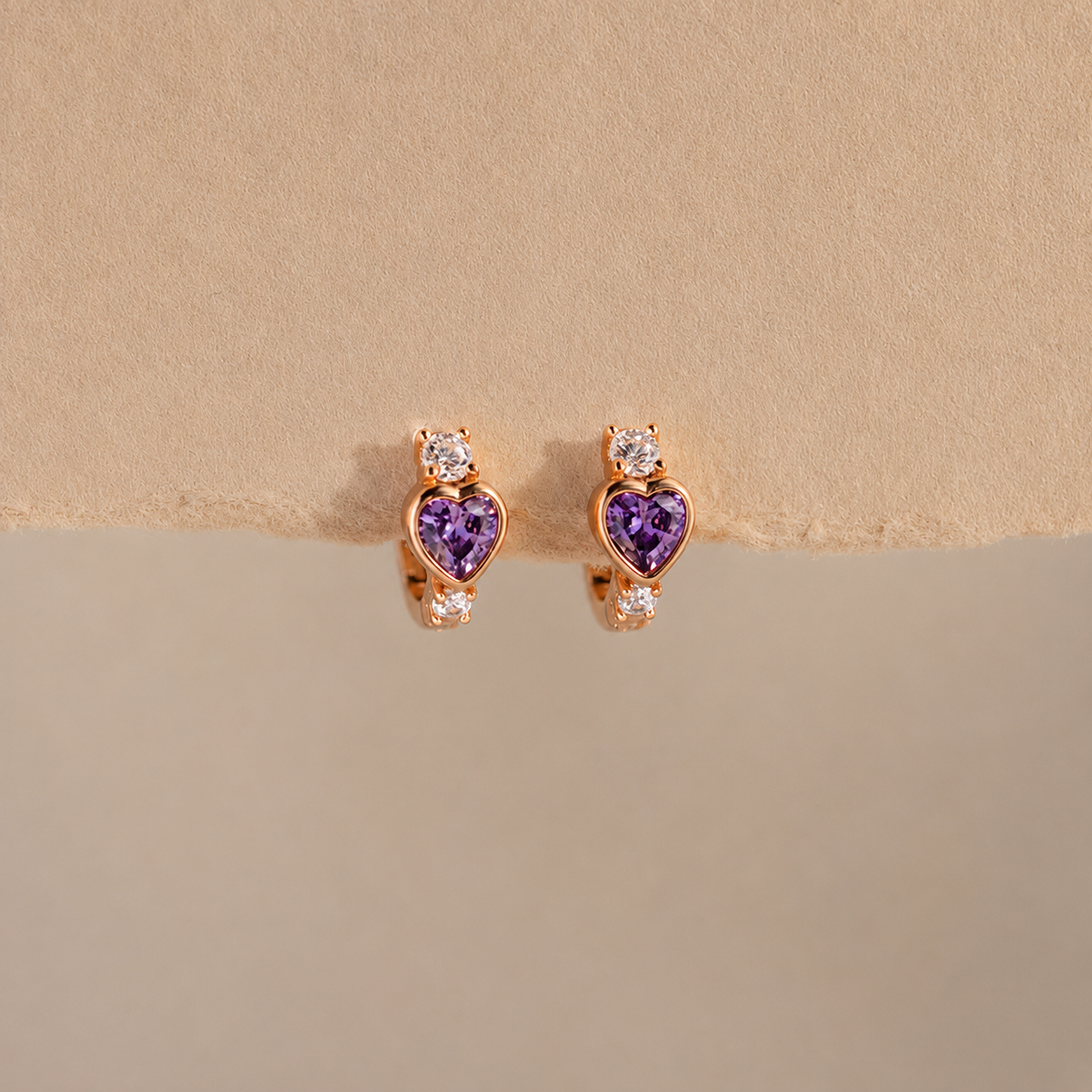 Heart-shaped purple gemstone earrings with rose gold setting on a beige background