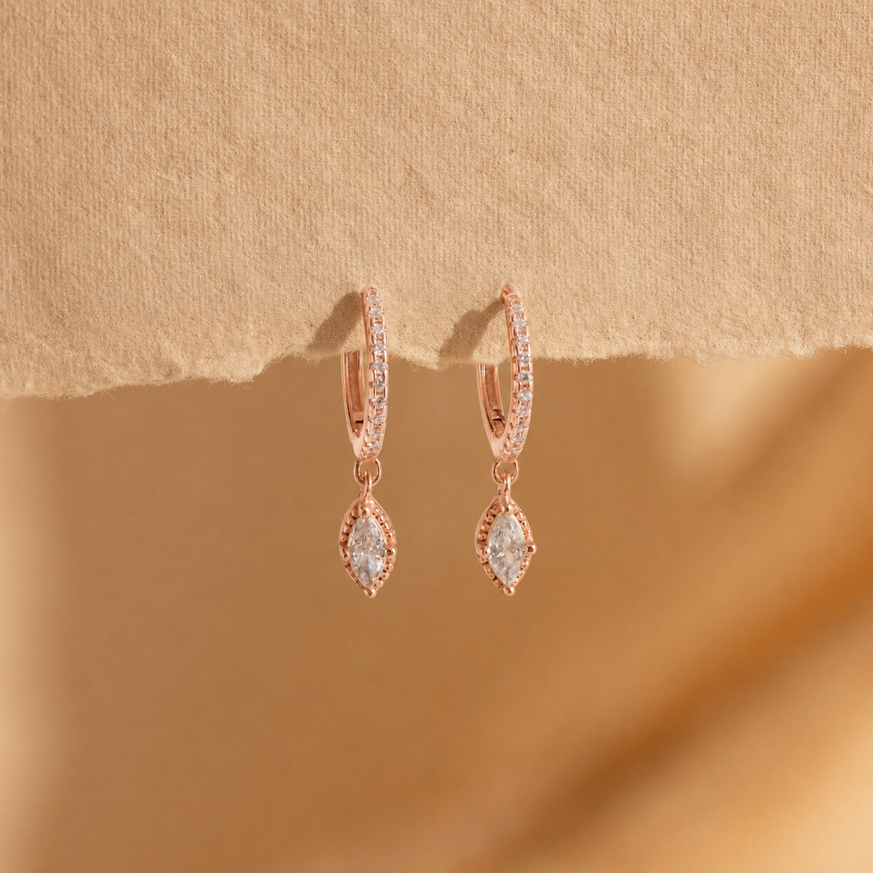 Rose gold earrings with clear gemstones on a beige background