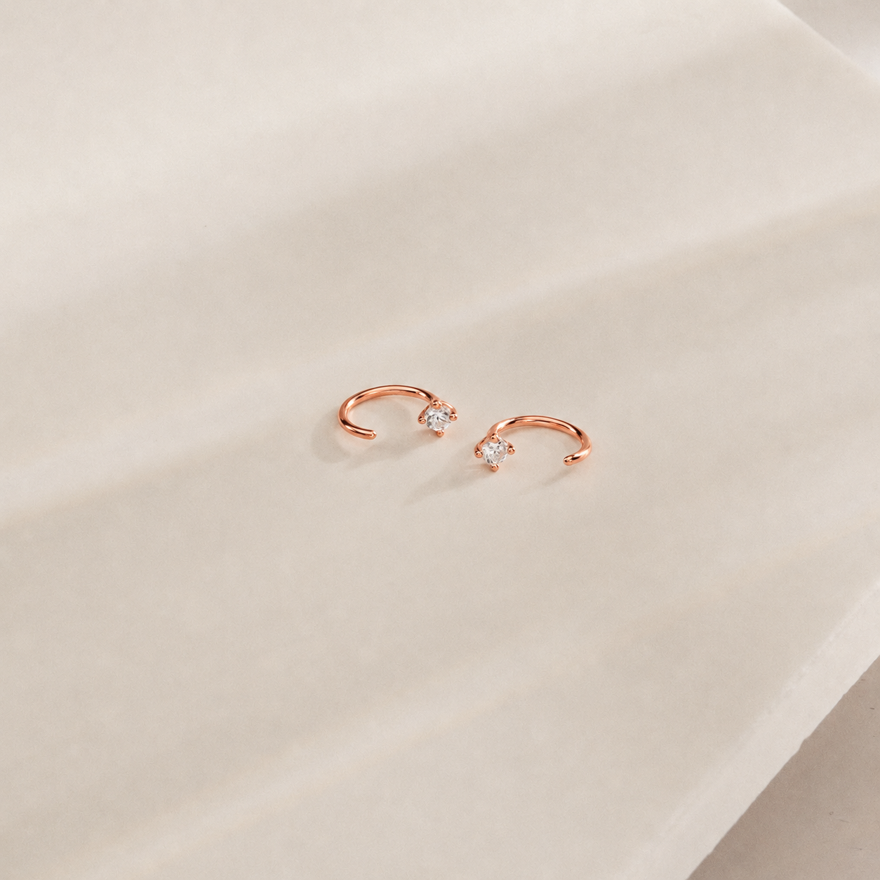 Rose gold earrings with small diamonds on a beige surface