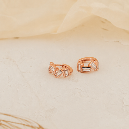 Rose gold earrings with geometric design on a beige fabric background
