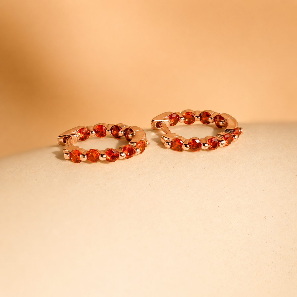 Pair of orange hoop earrings on a beige surface with a beige background
