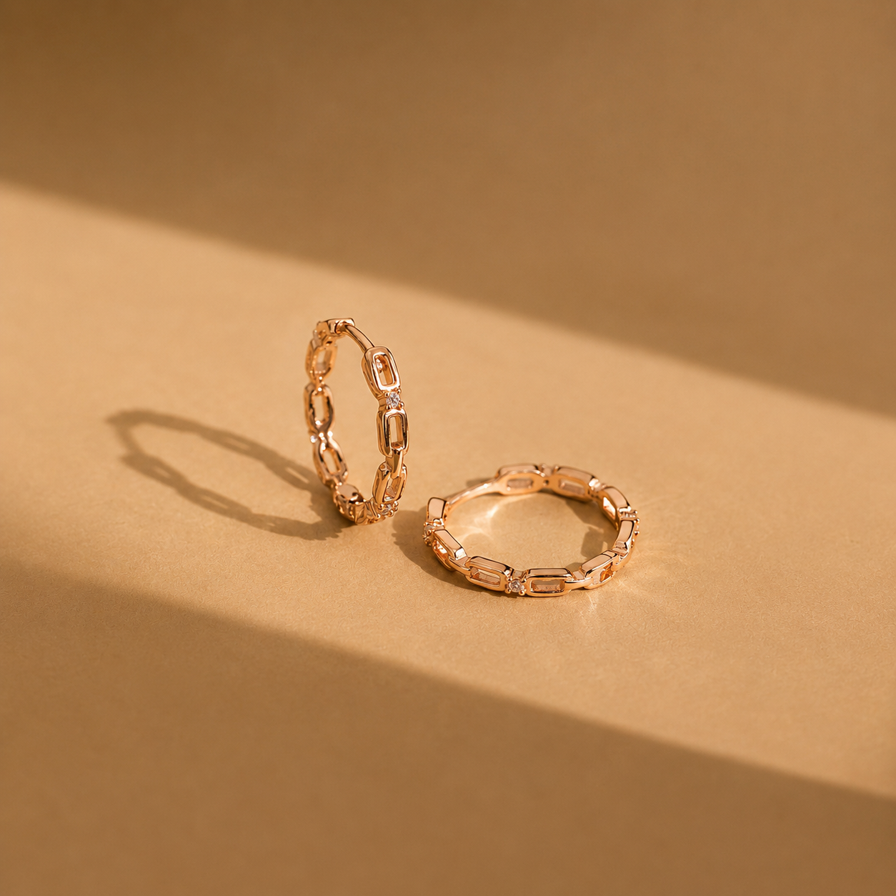 Two rose gold chain-style rings on a beige background