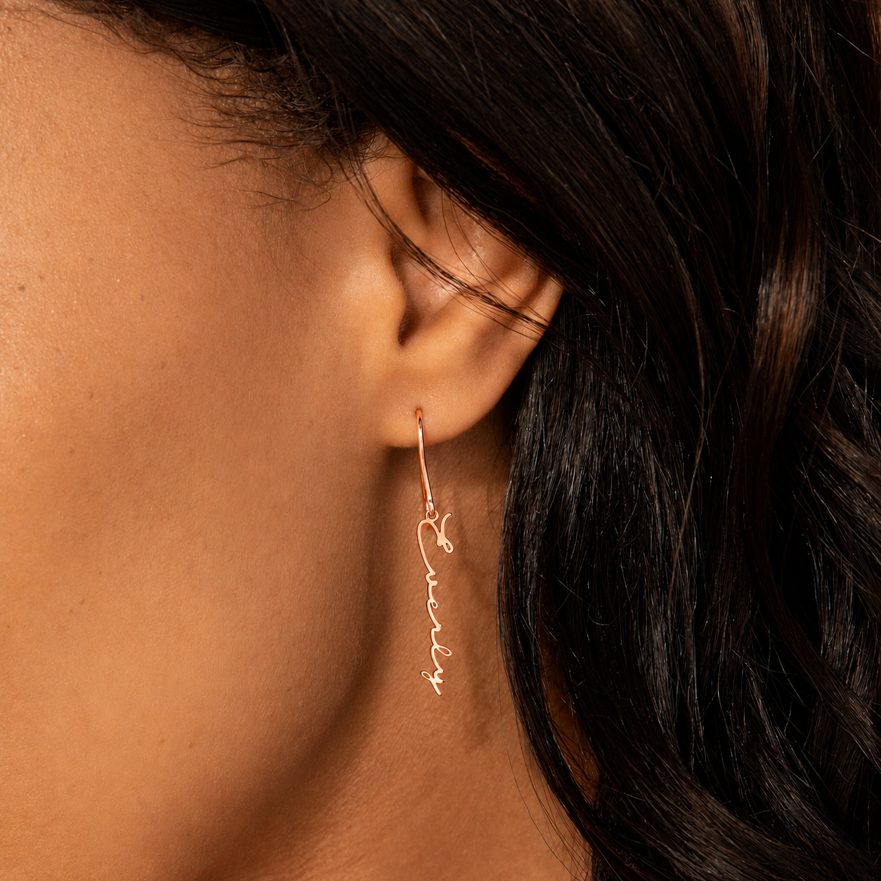 Close-up of an ear wearing a gold hoop earring with 'love' engraved.