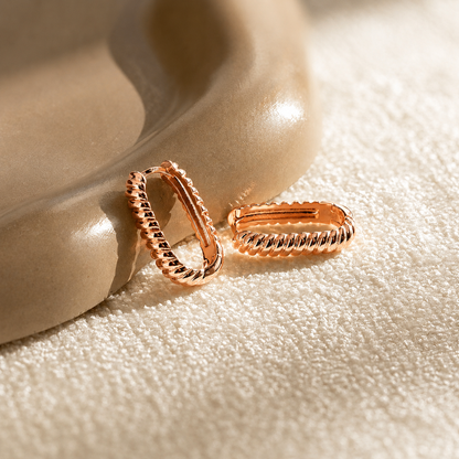 Rose gold hoop earrings on a textured beige surface