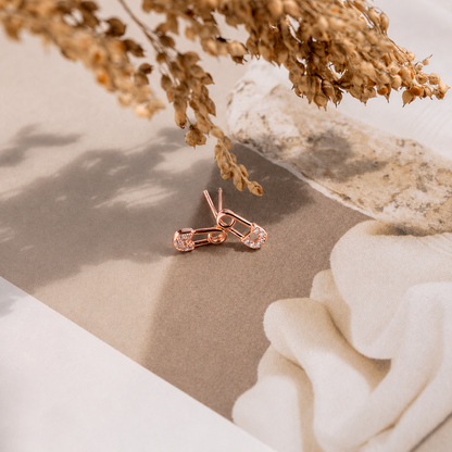 Rose gold earrings on a neutral surface with dried flowers and a white flower.