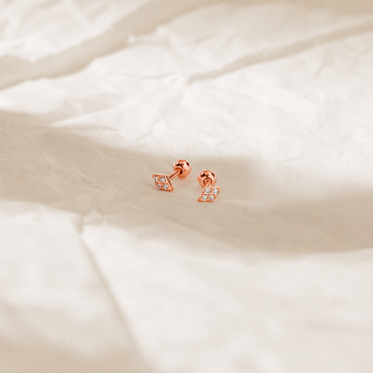 Rose gold earrings on a soft beige fabric background