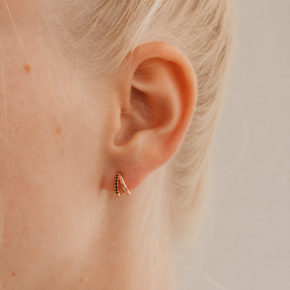 Close-up of an ear wearing a small hoop earring with a neutral background