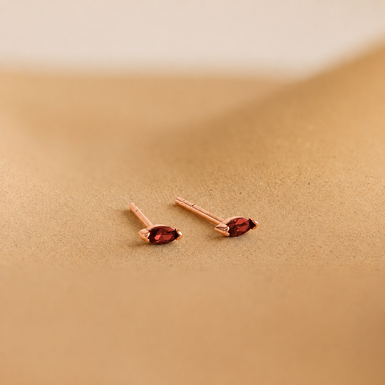 Pair of rose gold earrings with red gemstones on a beige background