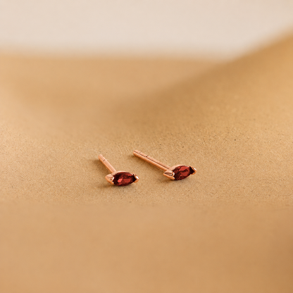 Pair of rose gold earrings with red gemstones on a beige background