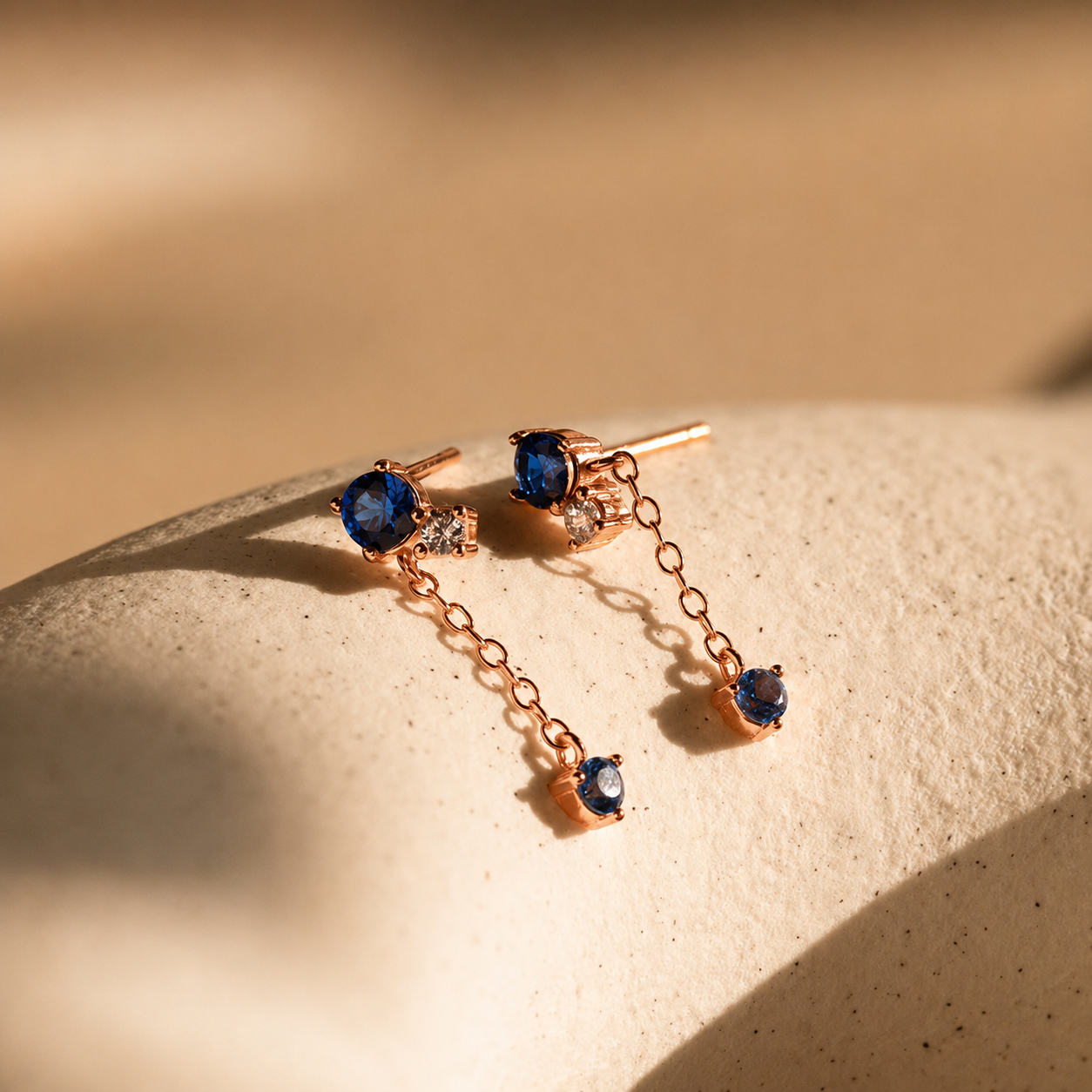 Rose gold earrings with blue gemstones on a beige surface